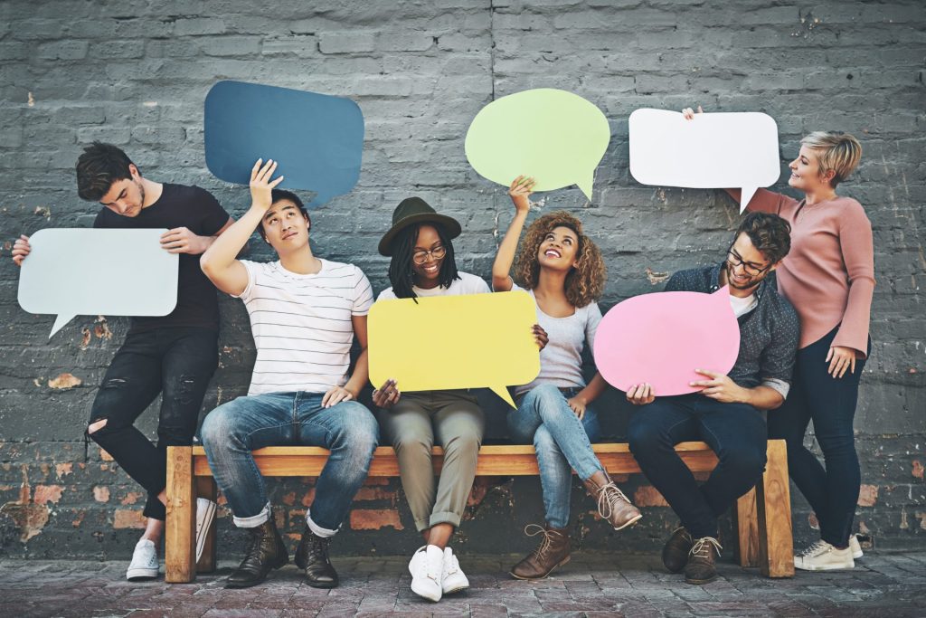 A group of people sitting on a bench holding speech bubble cards